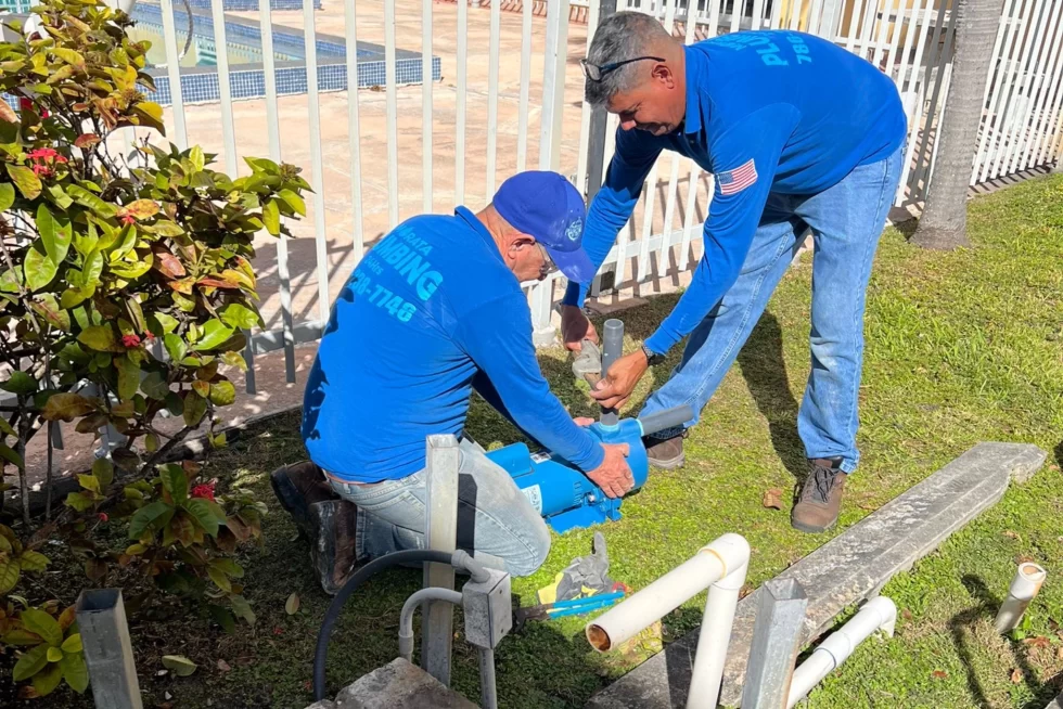 Licensed plumbers installing a booster pump and sewer line fittings at a Miami home