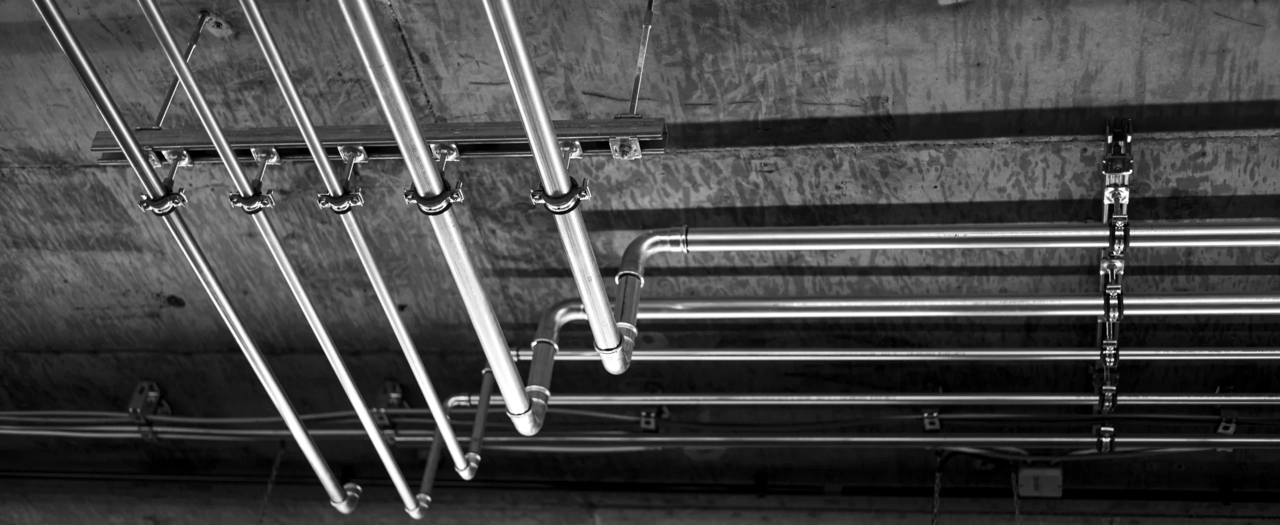 Parallel metal pipes mounted to concrete ceiling with brackets in commercial infrastructure setup.